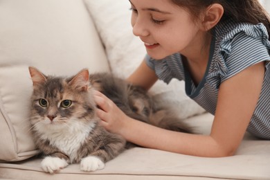 Photo of Cute little girl with cat on sofa at home, closeup. First pet
