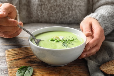 Woman eating fresh vegetable detox soup made of green peas at table, closeup