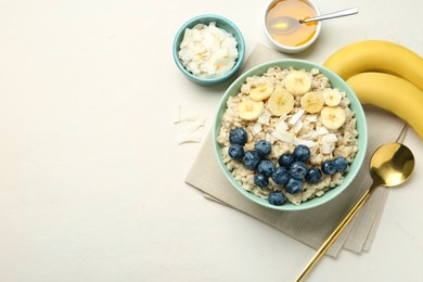 Photo of Tasty oatmeal with banana, blueberries, coconut flakes and honey served in bowl on beige table, flat lay. Space for text