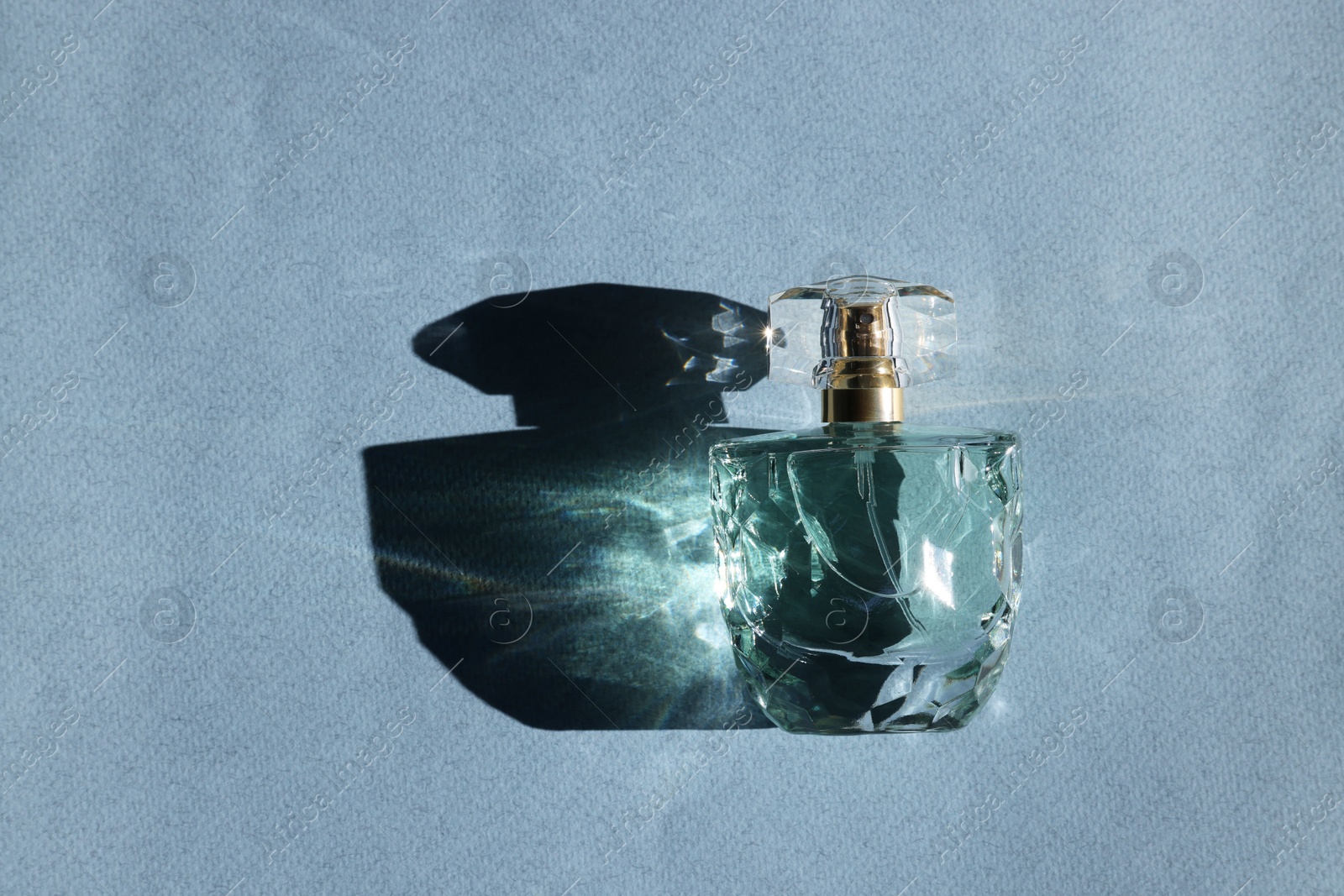 Photo of Luxury women's perfume. Sunlit glass bottle on grey background, top view. Space for text