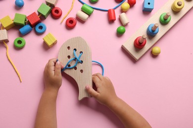 Photo of Motor skills development. Little child playing with wooden lacing toy at pink table, top view
