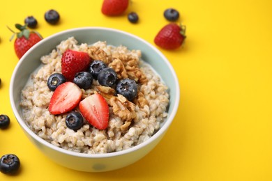 Photo of Tasty oatmeal with strawberries, blueberries and walnuts in bowl on yellow background. Space for text