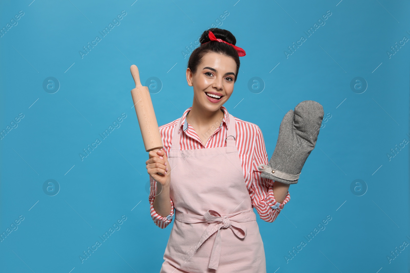 Photo of Young housewife in oven glove holding roller pin on light blue background