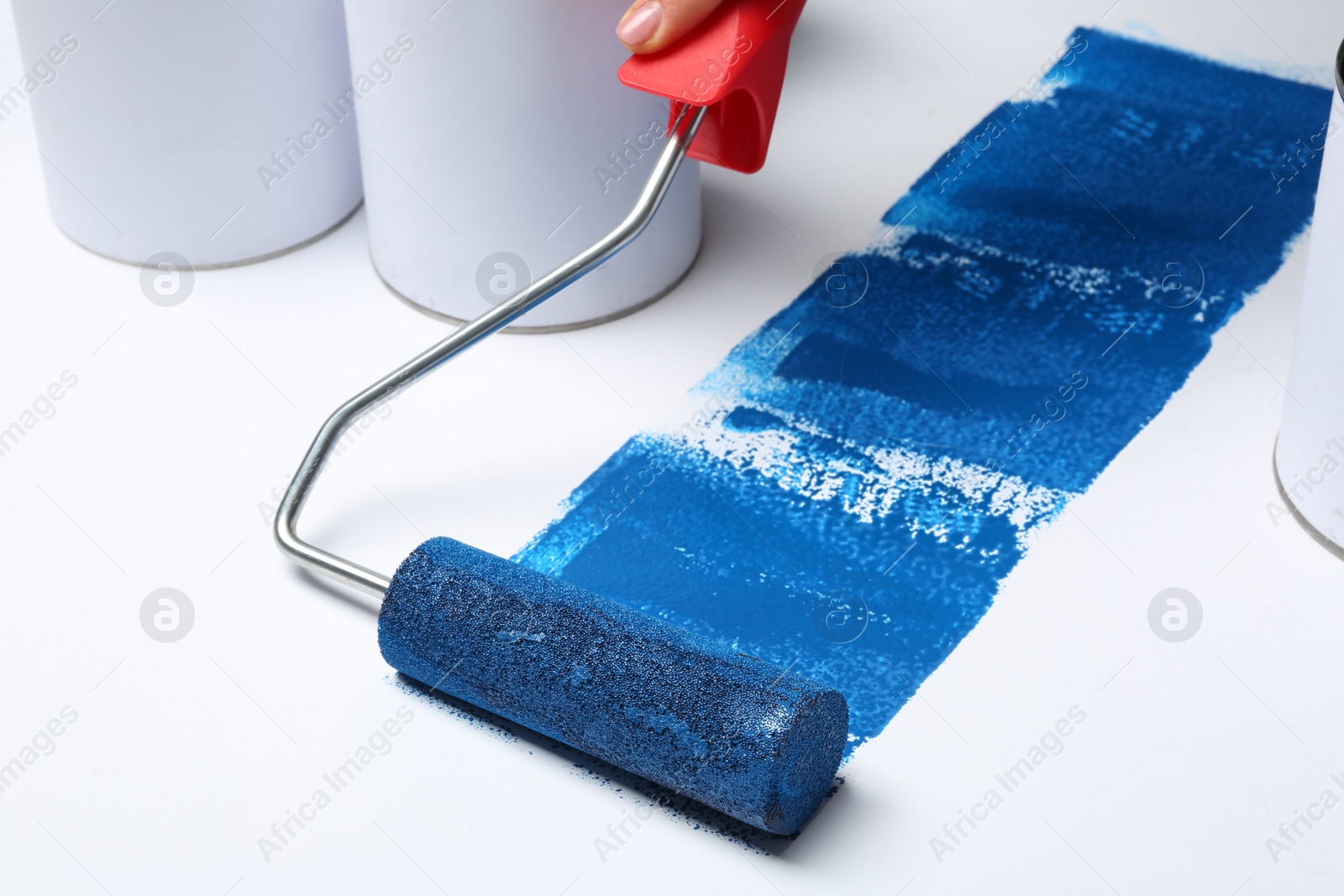Photo of Woman painting with roller brush near cans on white background, closeup