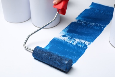 Photo of Woman painting with roller brush near cans on white background, closeup