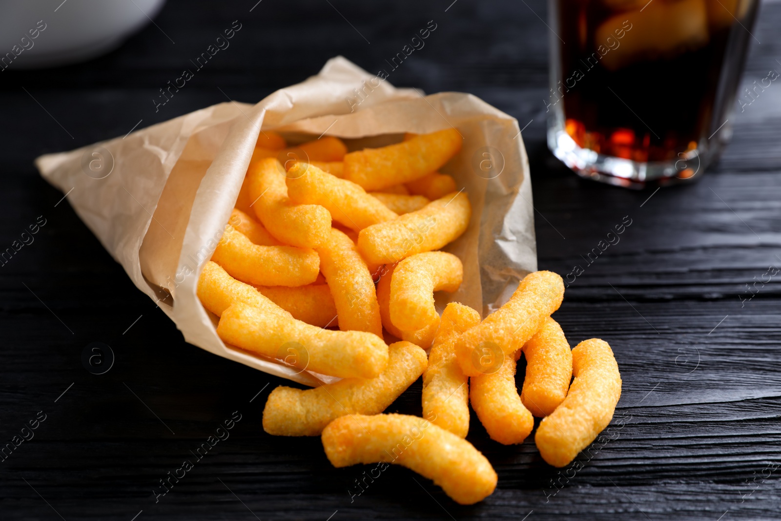 Photo of Crunchy cheesy corn snack on black wooden table, closeup