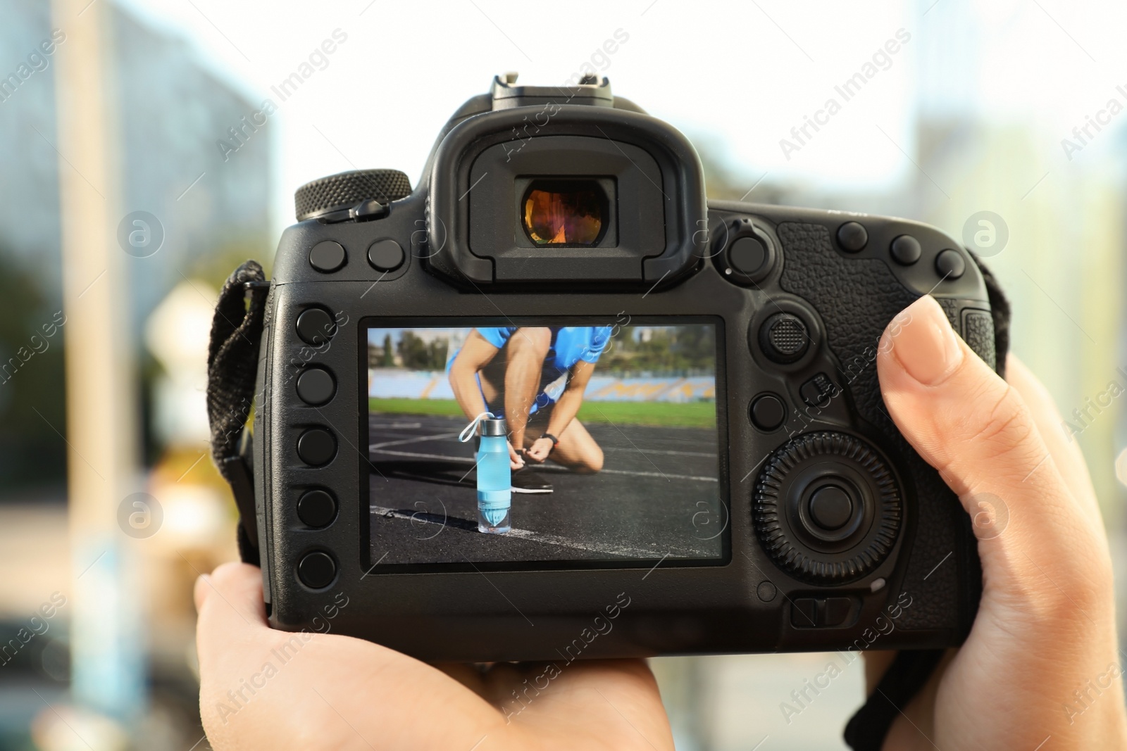 Photo of Female photographer holding professional camera with picture on screen outdoors, closeup