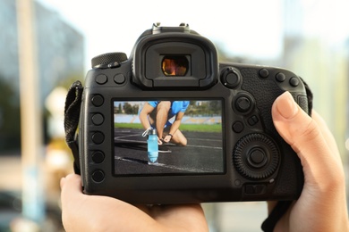 Photo of Female photographer holding professional camera with picture on screen outdoors, closeup