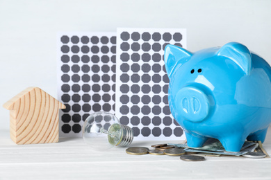 Photo of Composition with solar panels and piggy bank on white wooden table