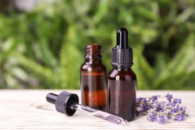 Photo of Bottles with natural lavender essential oil on white wooden table against blurred background. Space for text