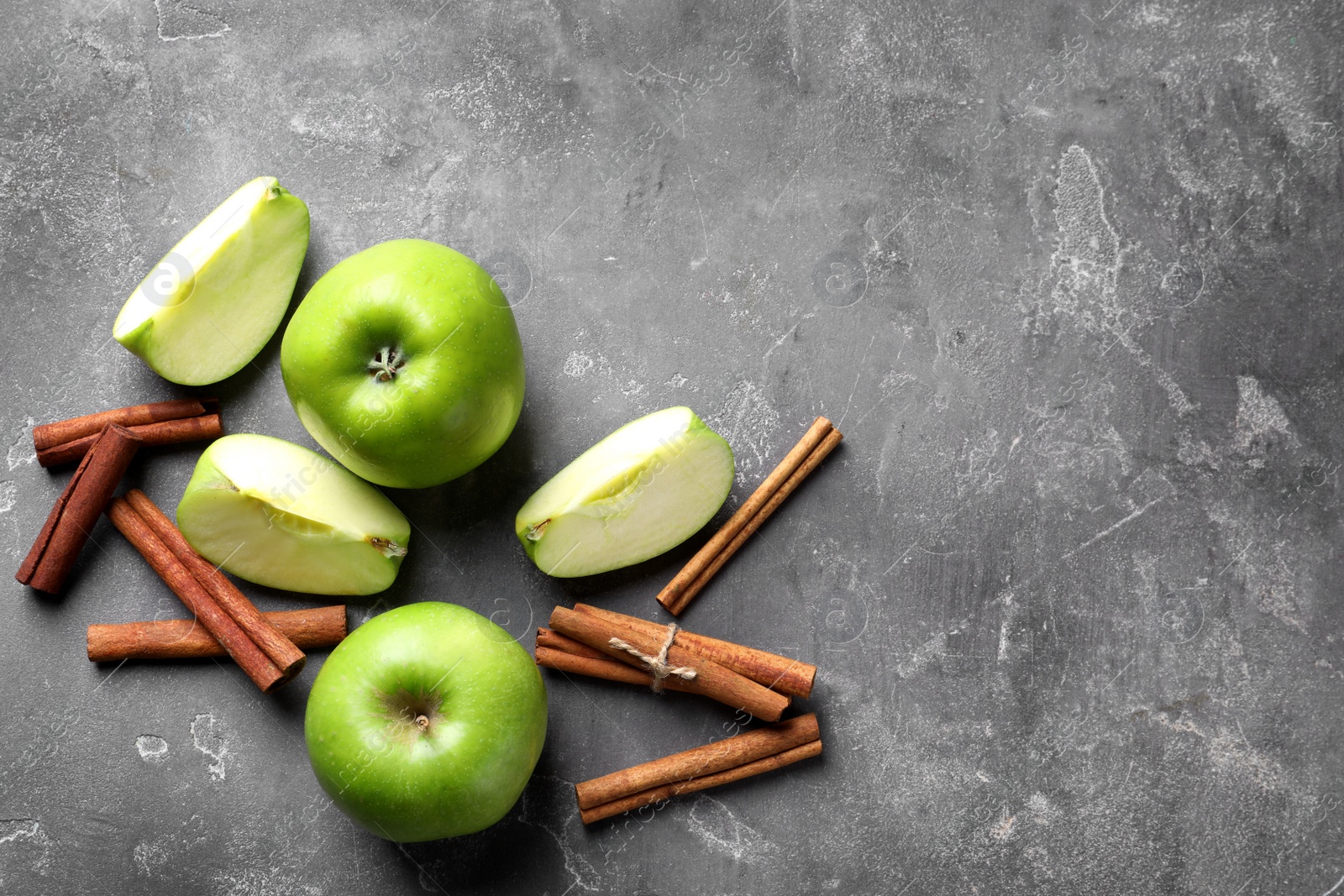 Photo of Fresh apples and cinnamon sticks on gray table, top view