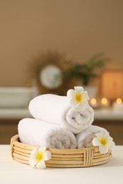 Photo of Spa composition. Rolled towels and plumeria flowers on white table indoors. Space for text