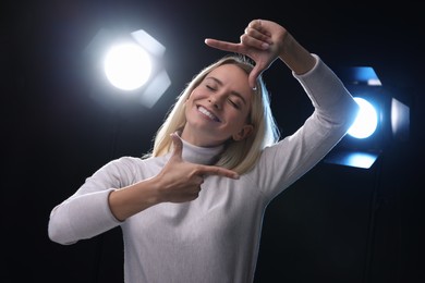Photo of Casting call. Emotional woman showing frame gesture on black background