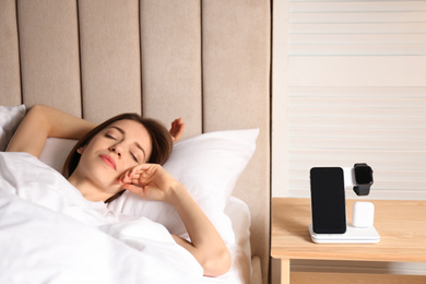 Photo of Smartphone, watch, earphones charging on wireless pad and sleeping woman in room