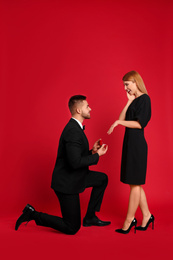 Photo of Man with engagement ring making marriage proposal to girlfriend on red background
