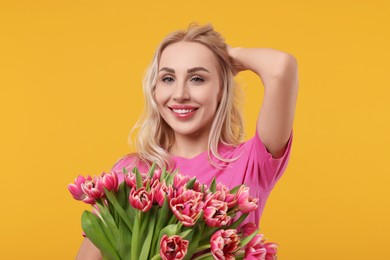 Happy young woman with beautiful bouquet on orange background