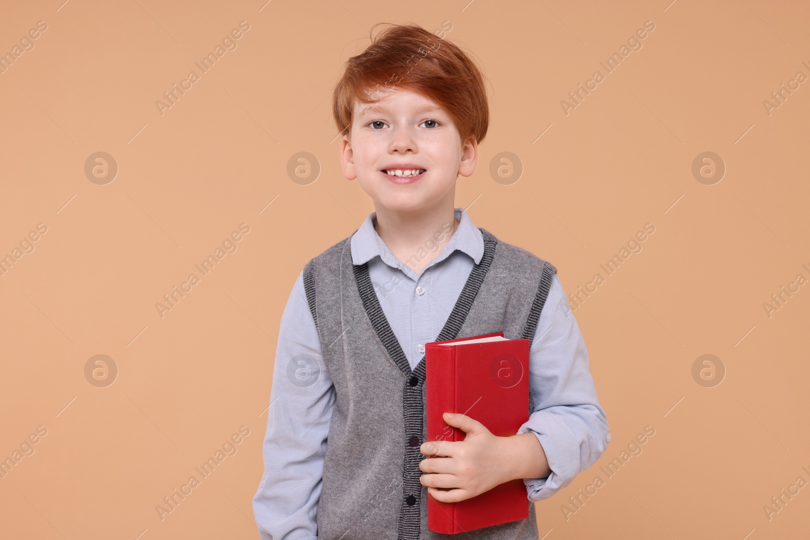 Photo of Smiling schoolboy with book on beige background