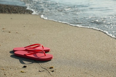 Photo of Stylish bright pink flip flops on sand near sea. Space for text