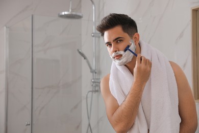 Photo of Handsome young man shaving with razor in bathroom, space for text