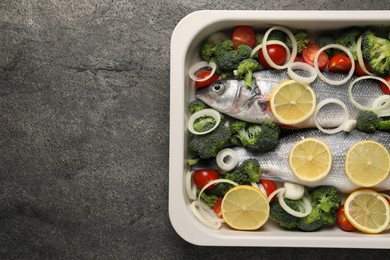 Raw fish with vegetables and lemon in baking dish on grey textured table, top view. Space for text