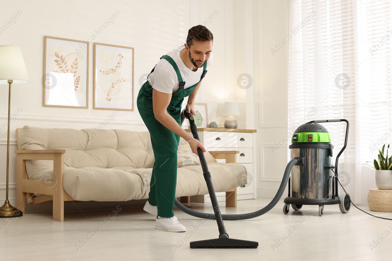 Photo of Professional janitor in uniform vacuuming floor indoors