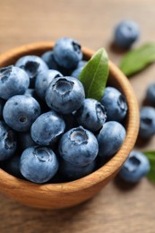 Photo of Bowl of tasty fresh blueberries with green leaves on wooden table, closeup