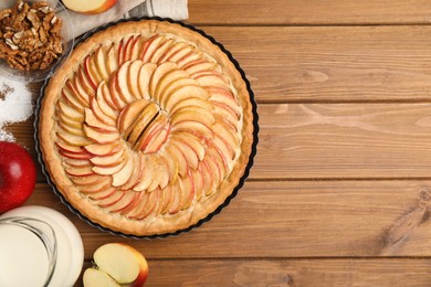 Delicious homemade apple tart and ingredients on wooden table, flat lay. Space for text