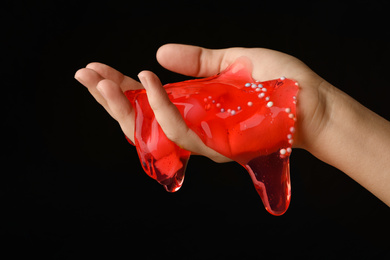 Photo of Woman playing with red slime on black background, closeup. Antistress toy