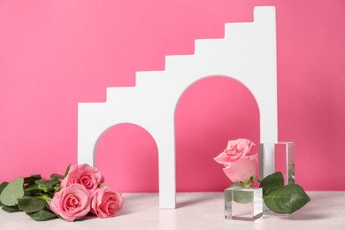 Photo of Stylish presentation for product. Geometric figures and beautiful roses on light table against pink background