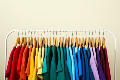 Rack with bright clothes on light background. Rainbow colors