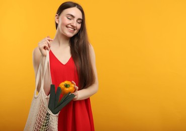 Photo of Woman with string bag of fresh vegetables on orange background, space for text