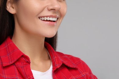 Photo of Young woman with clean teeth smiling on light grey background, closeup. Space for text