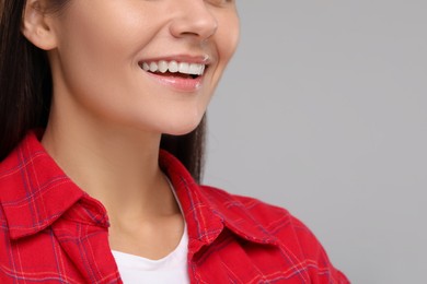 Young woman with clean teeth smiling on light grey background, closeup. Space for text