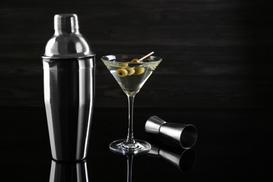 Photo of Metal shaker, Martini cocktail and jigger on black mirror surface