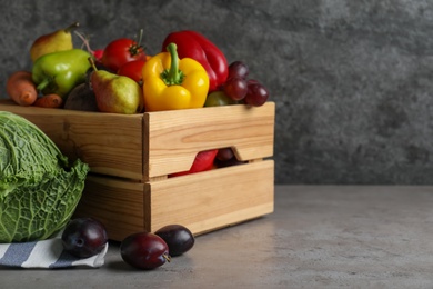 Photo of Wooden crate full of different vegetables and fruits on grey table, space for text. Harvesting time