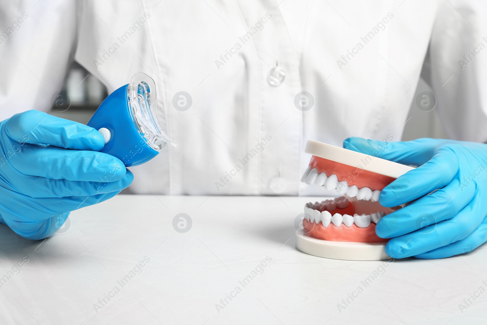 Photo of Dentist showing how to use teeth whitening device with educational model of oral cavity at table, closeup