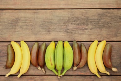 Many different bananas on wooden table, flat lay. Space for text