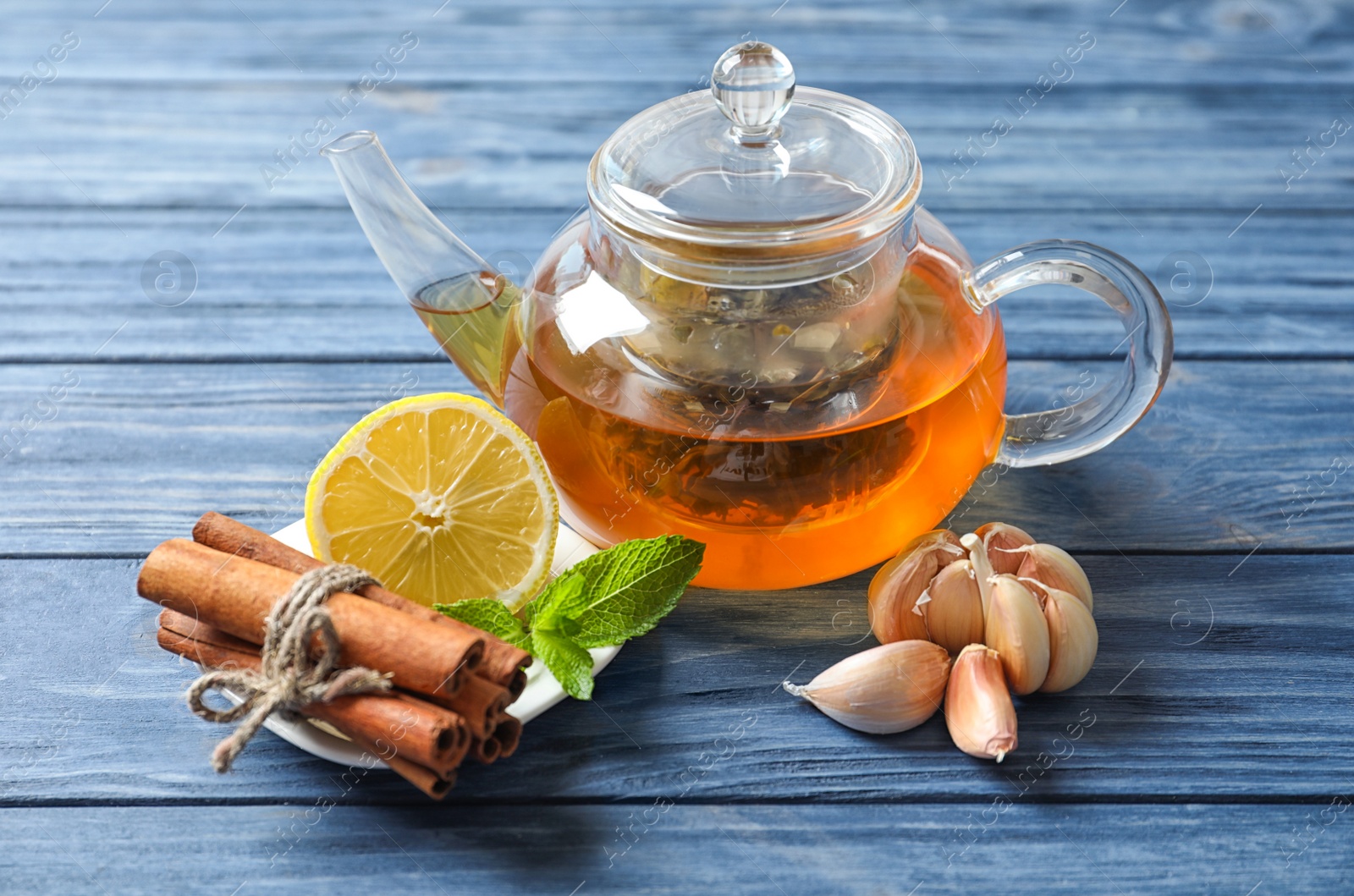 Photo of Glass teapot with hot tea, lemon and garlic as cold remedies on wooden table