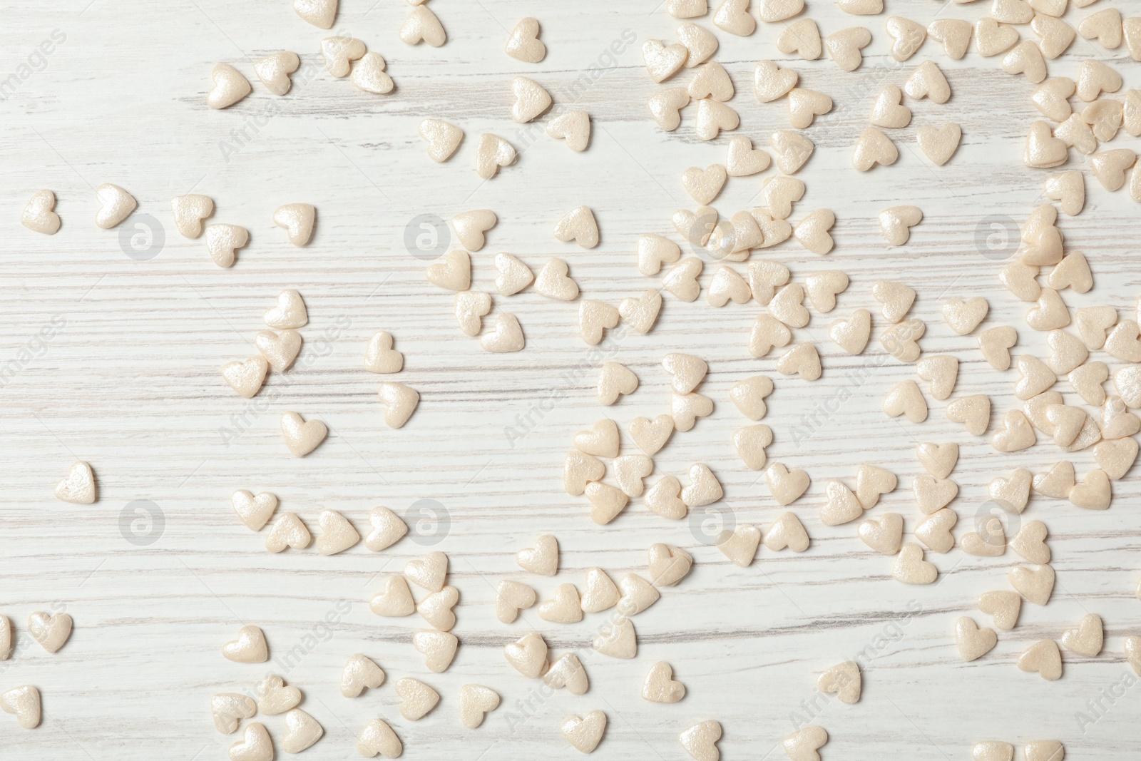 Photo of White heart shaped sprinkles on light wooden table, flat lay