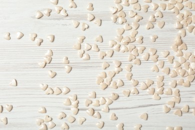 White heart shaped sprinkles on light wooden table, flat lay