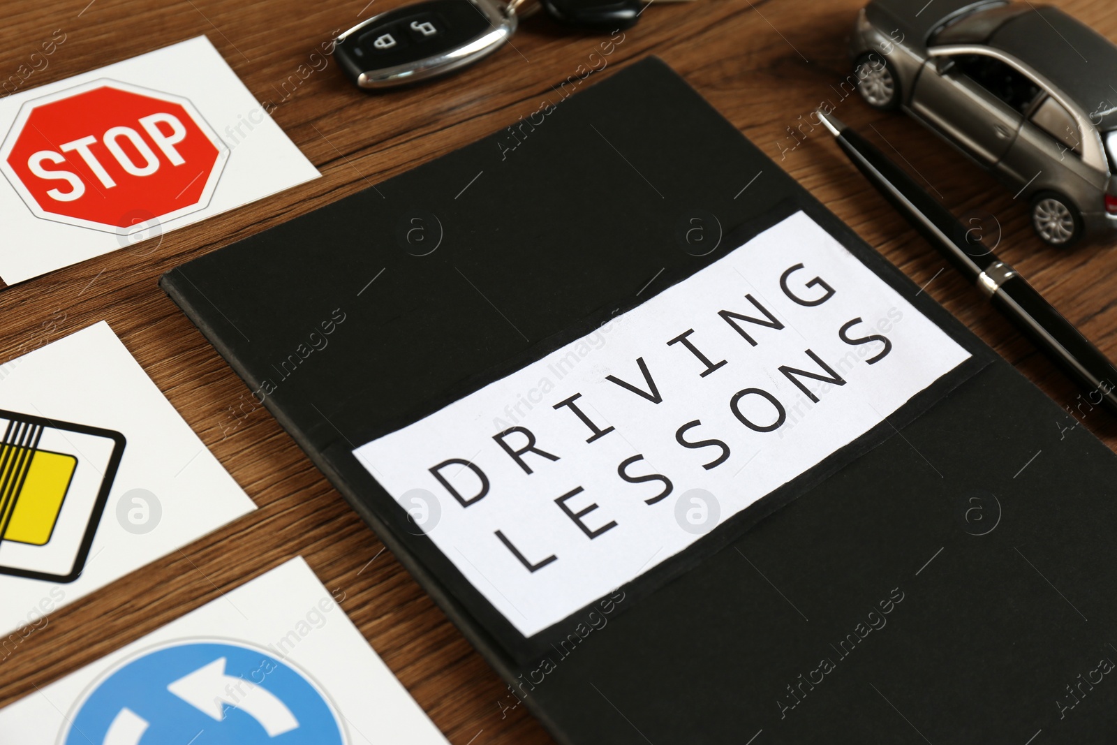 Photo of Workbook for driving lessons, pen and road signs on wooden table, closeup. Passing license exam