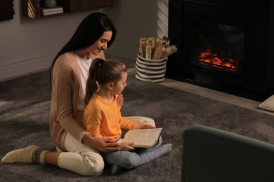 Photo of Happy mother and daughter reading together on floor near fireplace at home