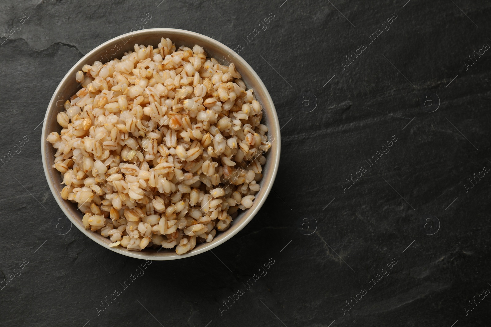 Photo of Tasty pearl barley porridge in bowl on dark textured table, top view. Space for text