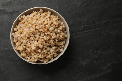 Photo of Tasty pearl barley porridge in bowl on dark textured table, top view. Space for text