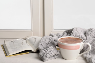 Photo of Composition with cup of hot chocolate and book on windowsill, space for text. Winter drink