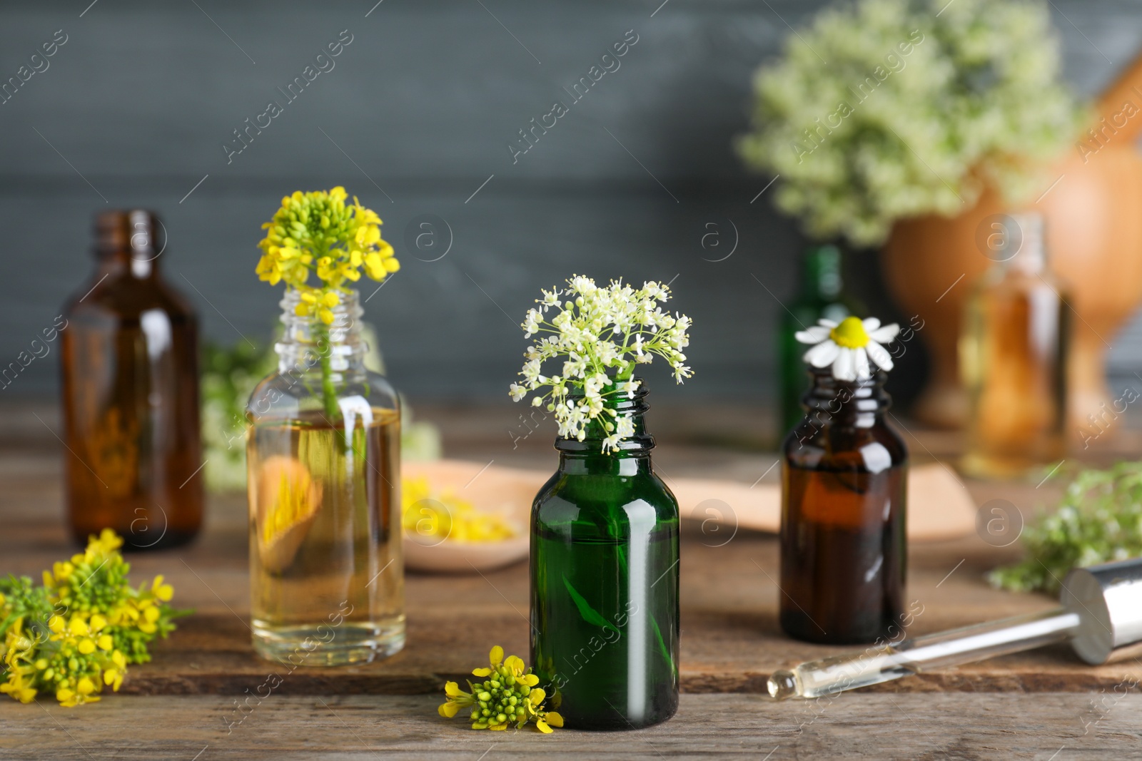 Photo of Bottles of essential oils, pipette and flowers on wooden table