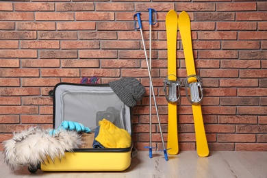 Suitcase with clothes, camera and skis on floor against brick wall. Winter vacation