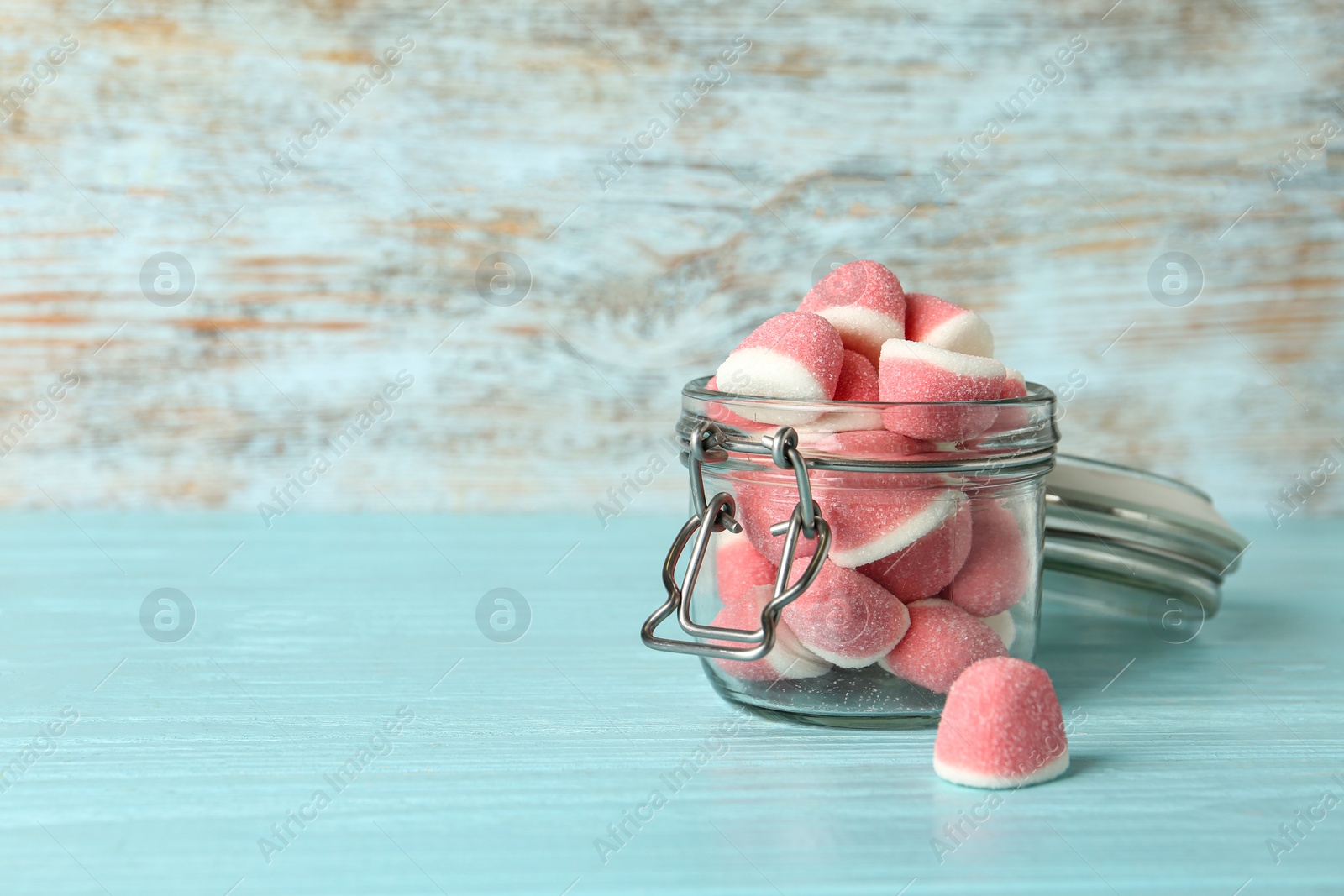 Photo of Glass jar with tasty jelly candies on blue table against wooden background, space for text