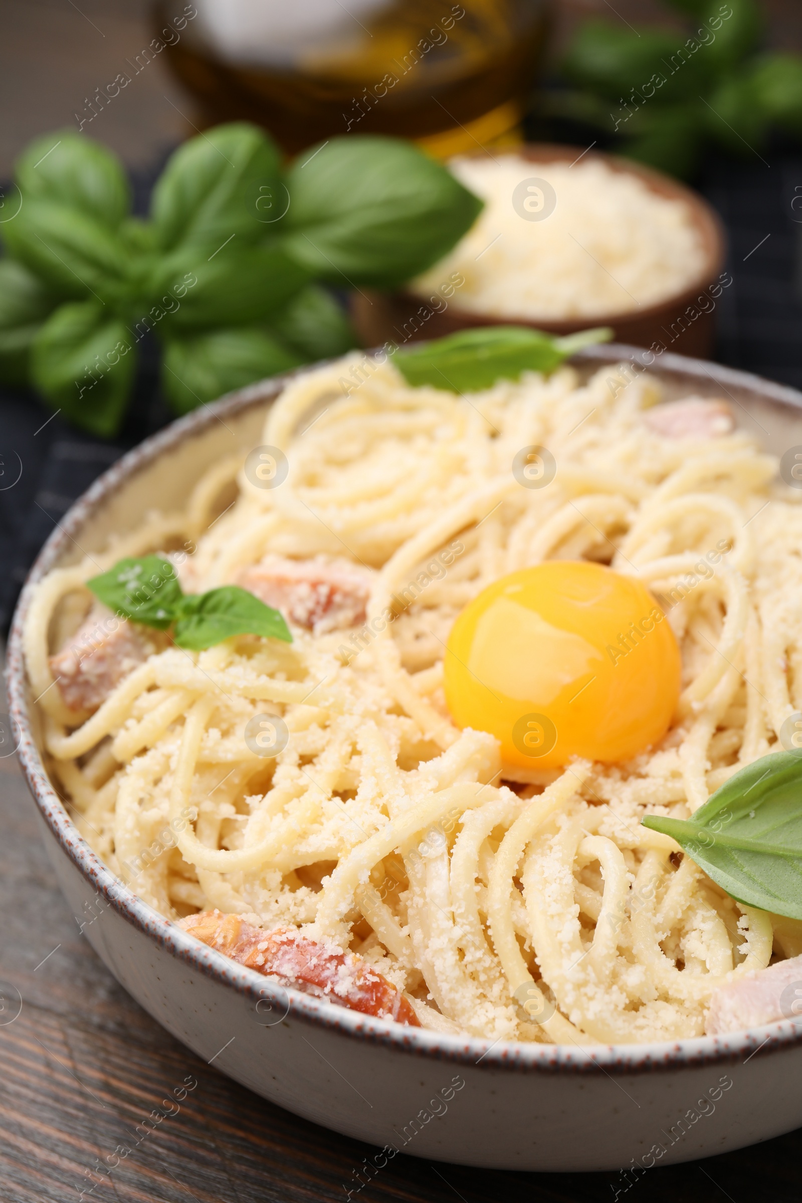 Photo of Bowl of tasty pasta Carbonara with basil leaves and egg yolk on wooden table, closeup