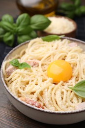 Photo of Bowl of tasty pasta Carbonara with basil leaves and egg yolk on wooden table, closeup